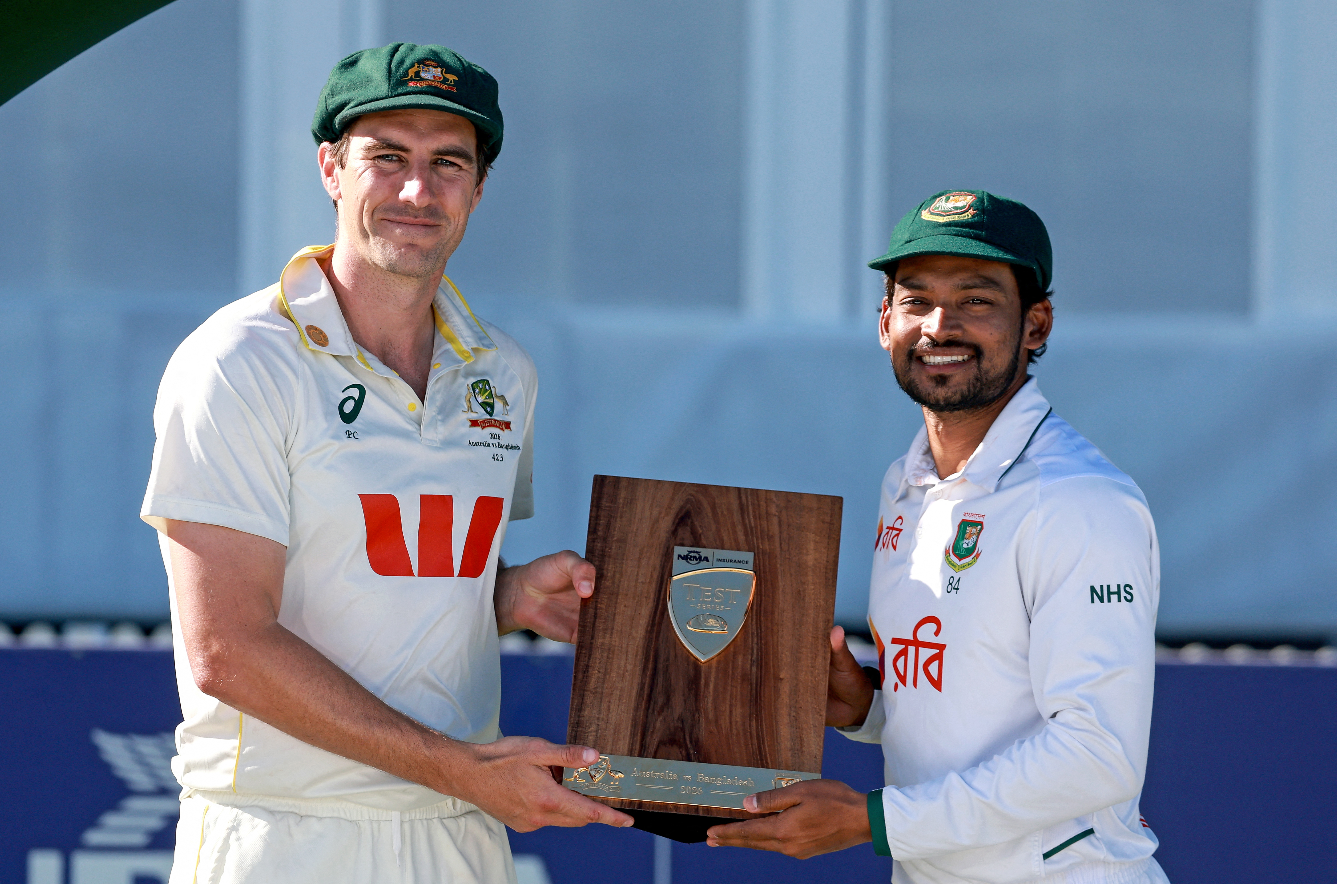 Australias captain Pat Cummins (L) holds the series trophy with Bangladeshs Bangladeshs Najmul Hossain Shanto (R) after the second day of the second cricket Test match between Australia and Bangladesh at the Great Barrier Reef Stadium in Mackay on August 23, 2026. (Photo by DAVID GRAY / AFP) / -- IMAGE RESTRICTED TO EDITORIAL USE - STRICTLY NO COMMERCIAL USE -- / The erroneous mention[s] appearing in the metadata of this photo by DAVID GRAY has been modified in AFP systems in the following manner: [Australias captain Pat Cummins] instead of [Australias Mitchell Starc]. Please immediately remove the erroneous mention[s] from all your online services and delete it (them) from your servers. If you have been authorized by AFP to distribute it (them) to third parties, please ensure that the same actions are carried out by them. Failure to promptly comply with these instructions will entail liability on your part for any continued or post notification usage. Therefore we thank you very much for all your attention and prompt action. We are sorry for the inconvenience this notification may cause and remain at your disposal for any further information you may require.