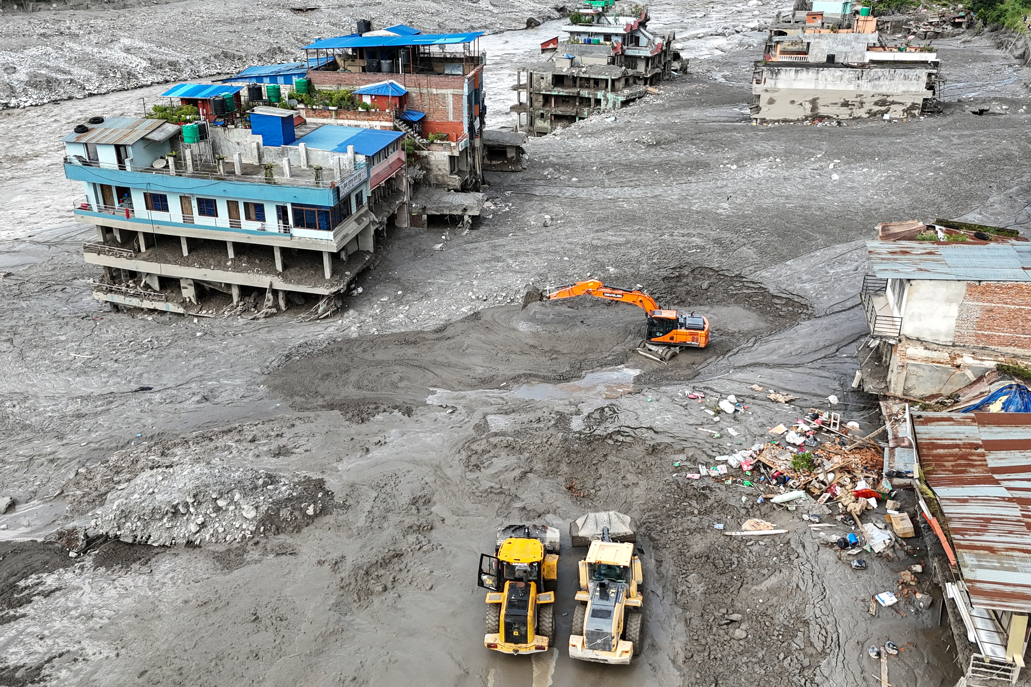 An aerial view shows workers using excavators to clear sludge following flash floods at Trishuli in Nepal’s Nuwakot district on August 27, 2026