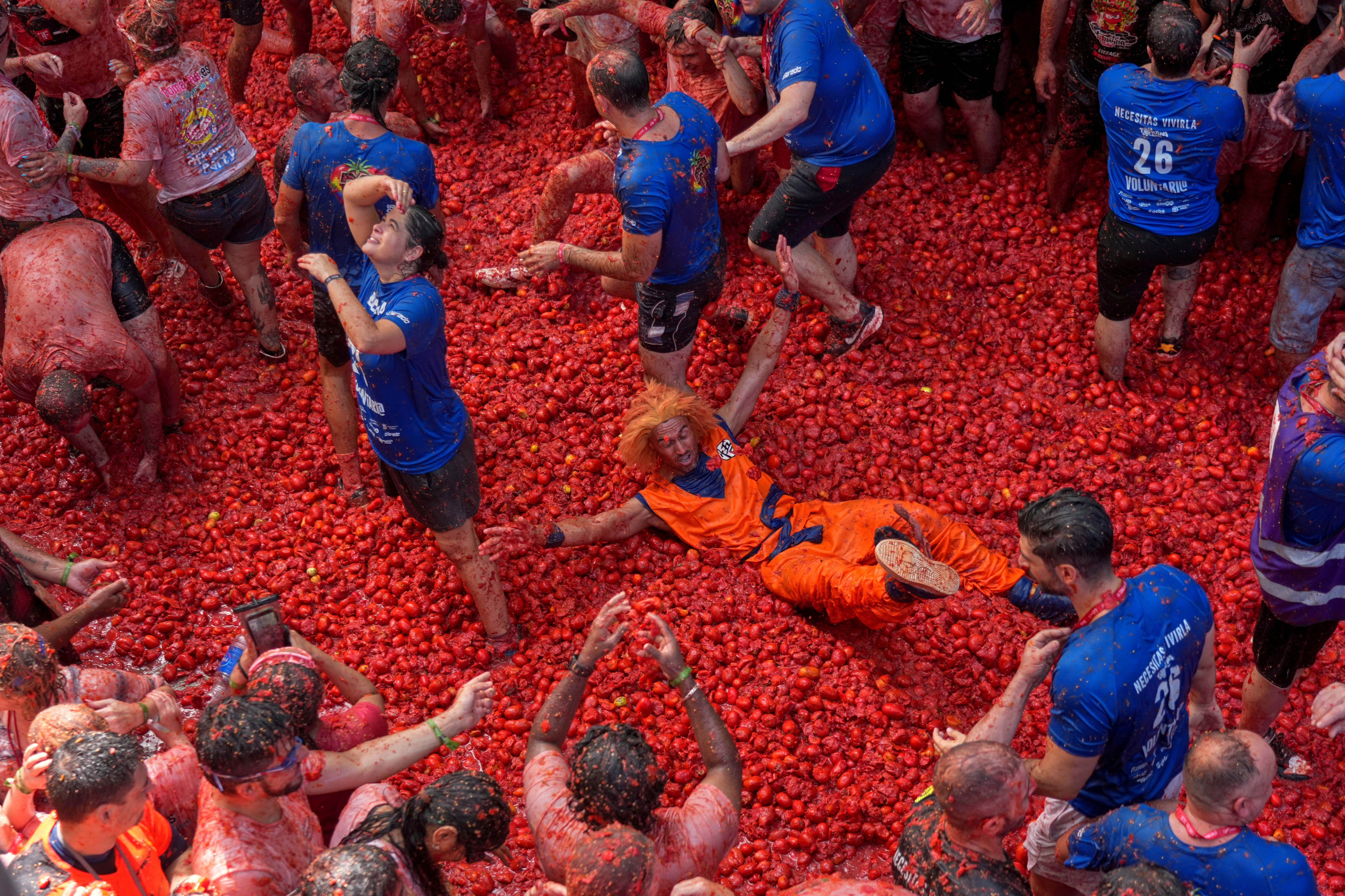 People stand and lie on a huge pile of tomatoes.