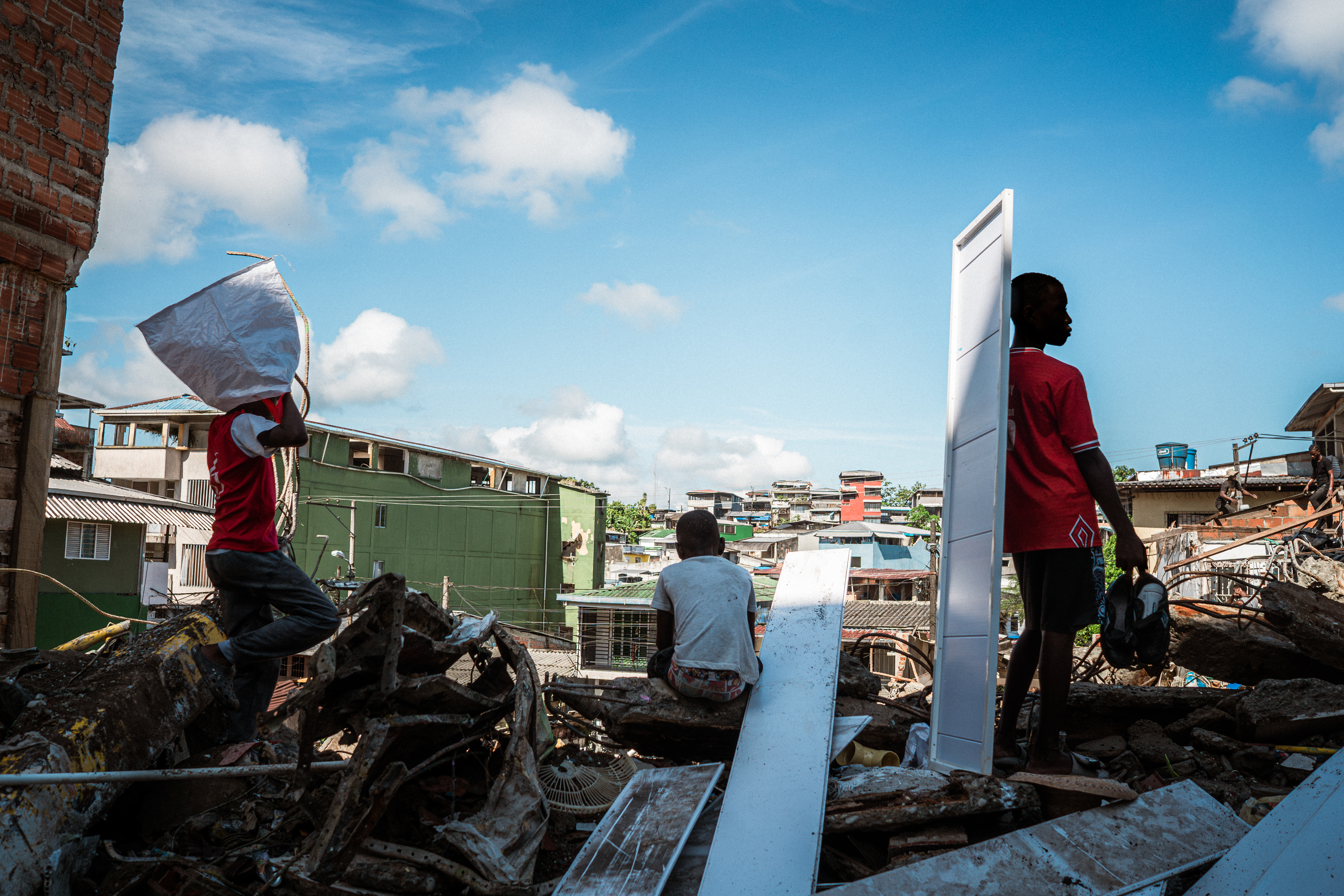 Beneath the ruins of Lorena Hipis’s home, a group of young boys kick their way through the debris. [Euan Wallace / Al Jazeera]