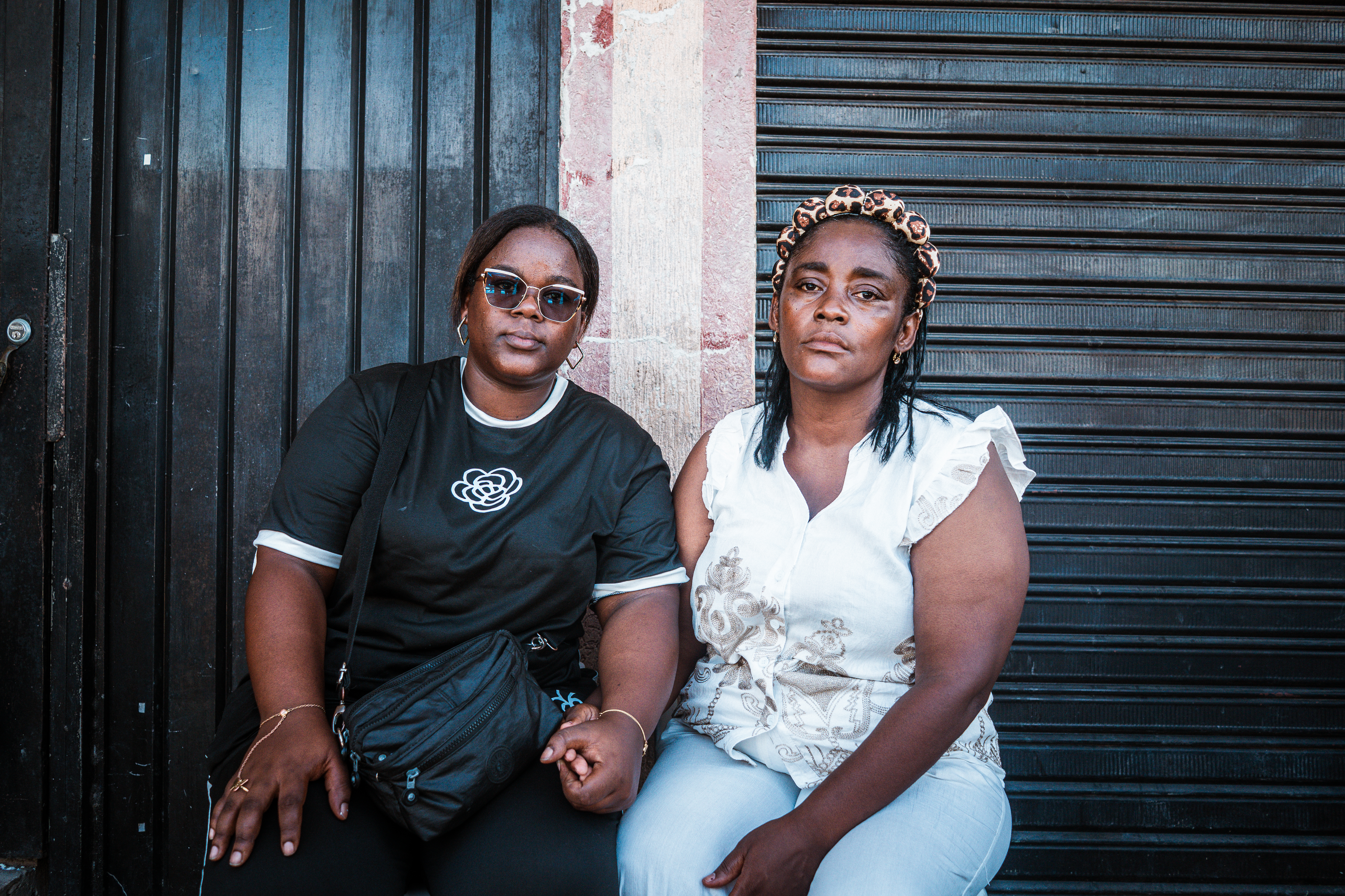 Sitting opposite the wreckage of their home in Barrio Oriente, Betsy Tenorio [left] grasps her mothers hand. Tonorio’s grandfather was killed when the building collapsed during the earthquake. [Euan Wallace / Al Jazeera]