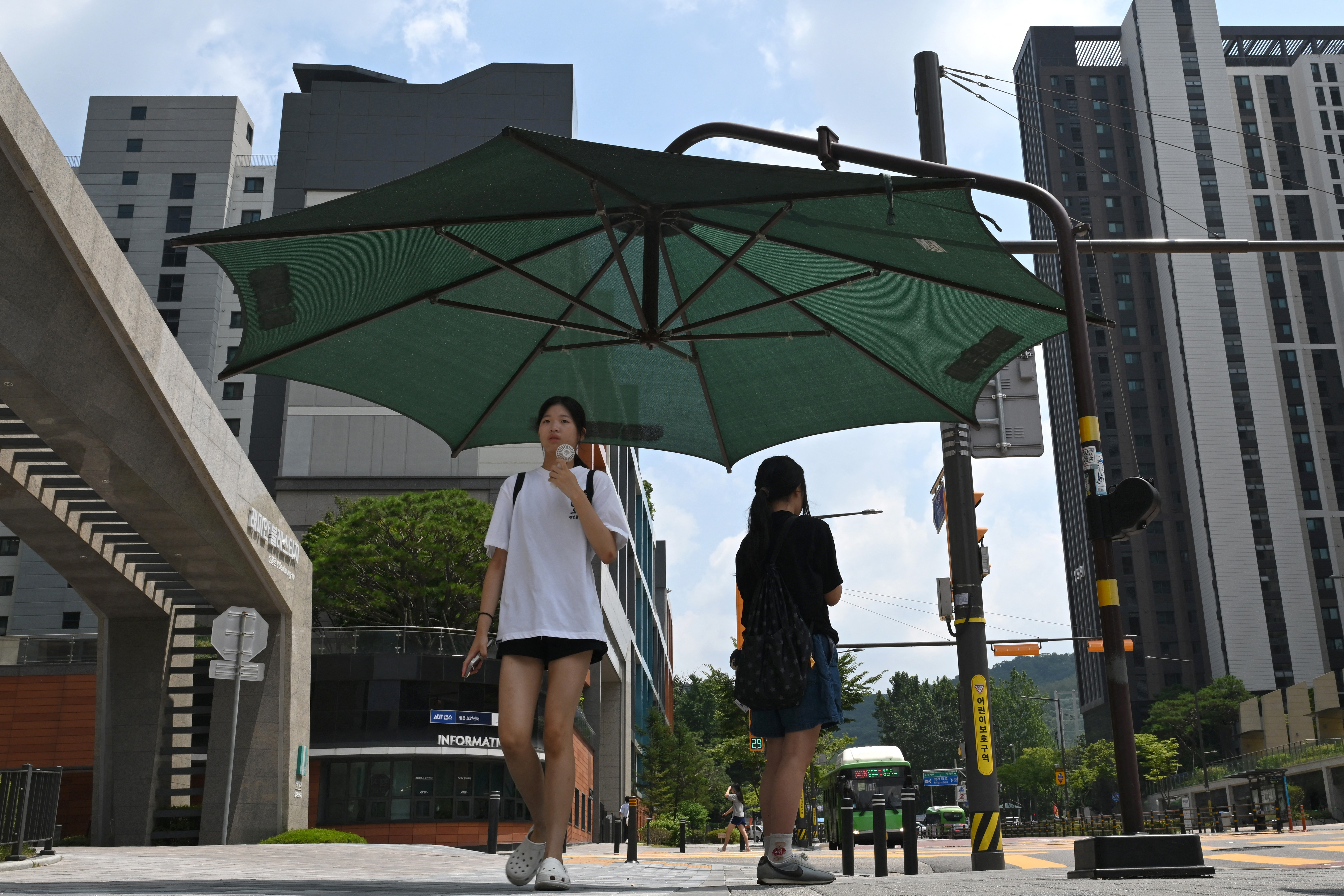 TOPSHOT - Pedestrians stand under a shade shelter at Gangnam district in Seoul on August 4, 2026, as a scorching heatwave continues to grip South Korea.