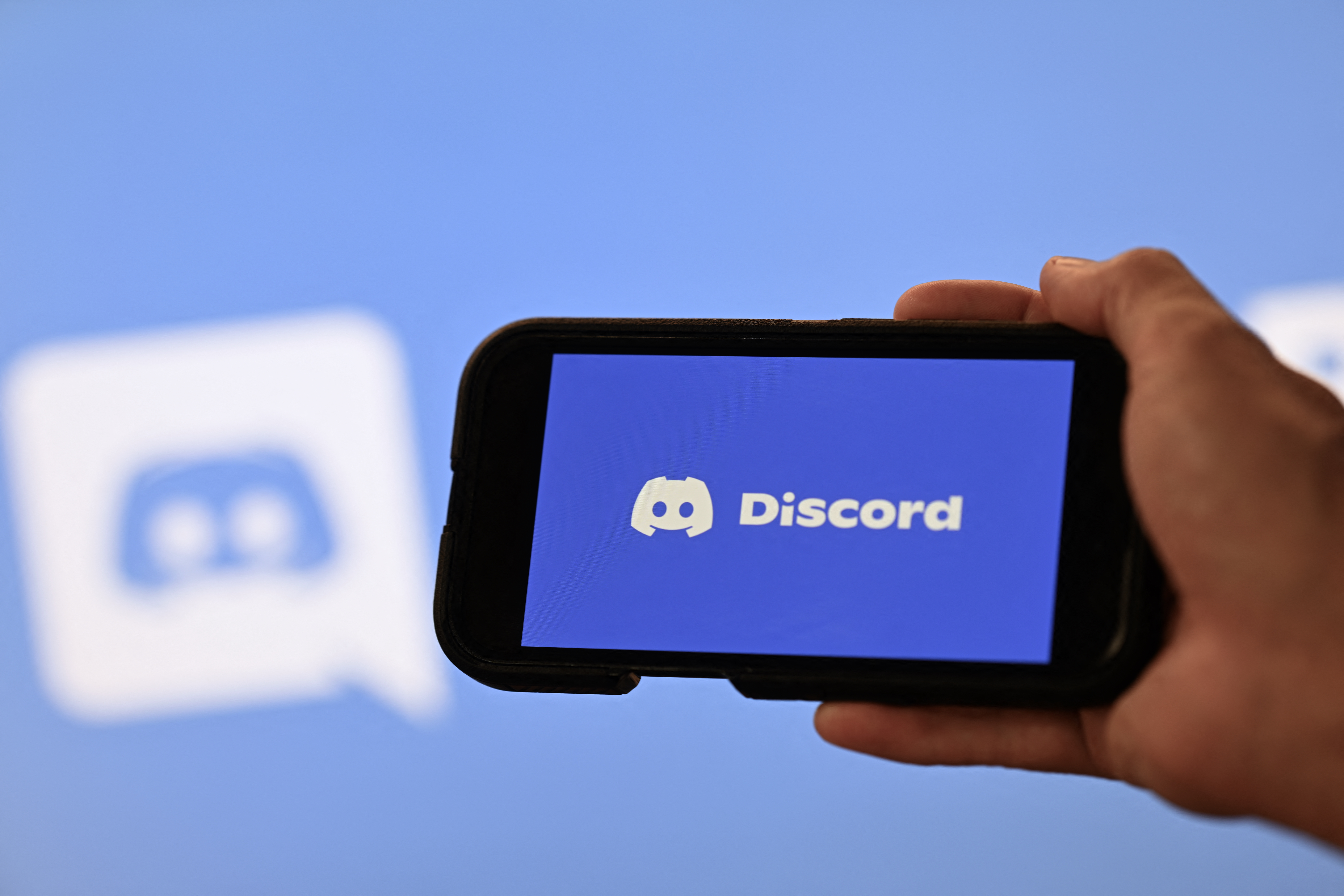 This photo illustration shows a hand holding a smartphone in front of a screen displaying the logo of the US company Discord in Rio de Janeiro, Brazil, on August 12, 2026.