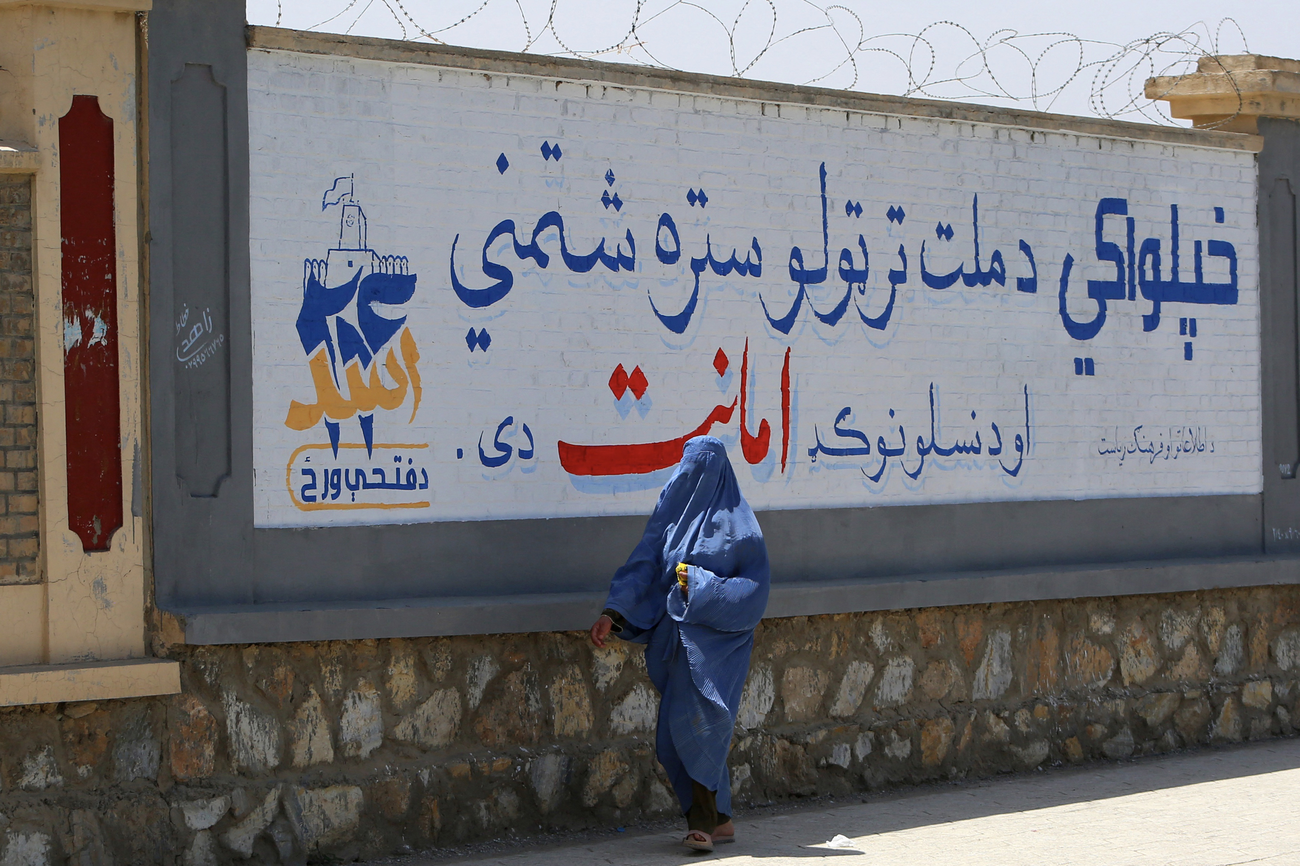 An Afghan burqa-clad woman walks past a mural commemorating the fifth anniversary marking the Taliban's return to power, in Afghanistan's Ghazni province on August 13, 2026. [AFP]