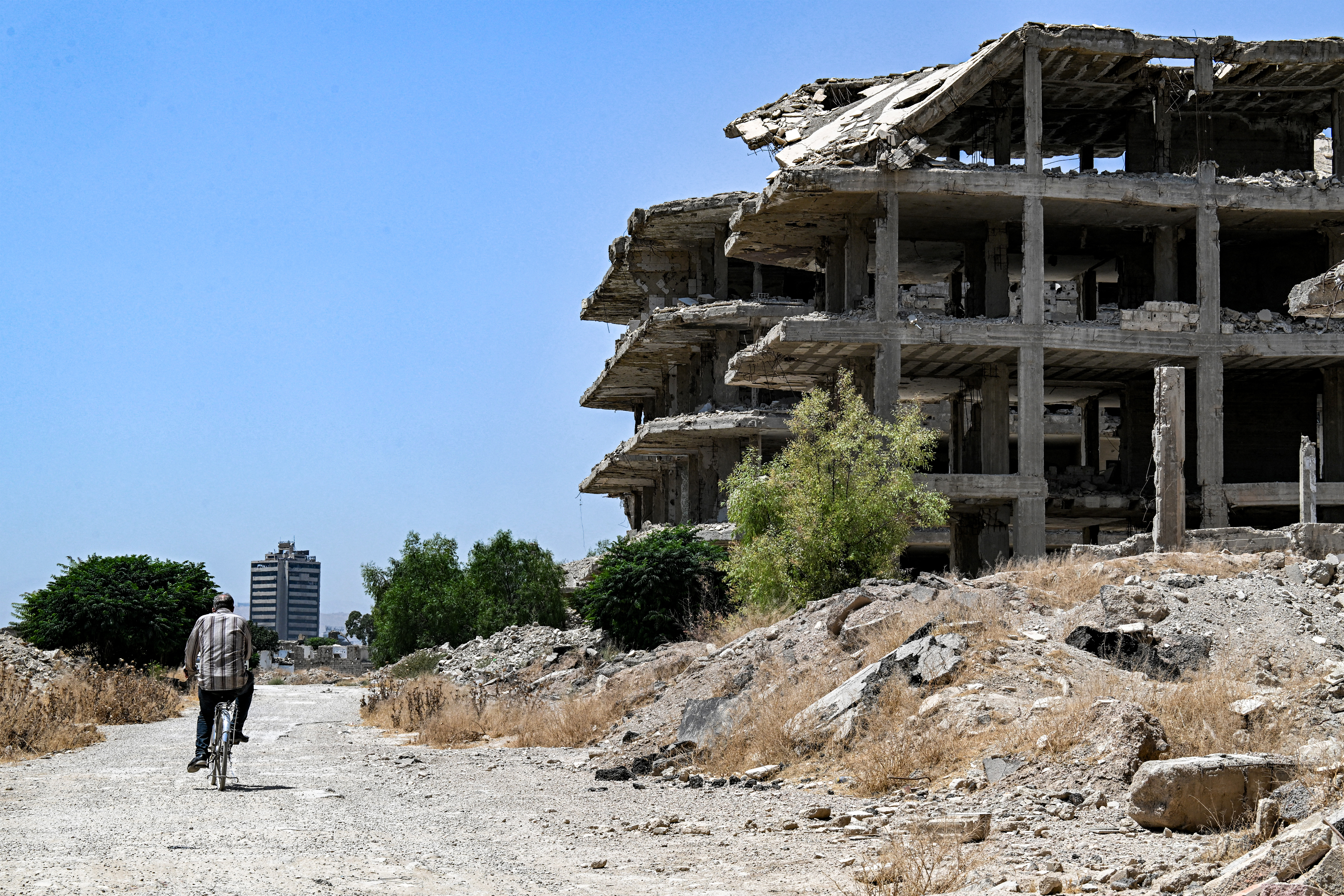 A man cycles past heavily-damaged and destroyed buildings in the Jobar suburb northeast of Damascus on August 12, 2026.