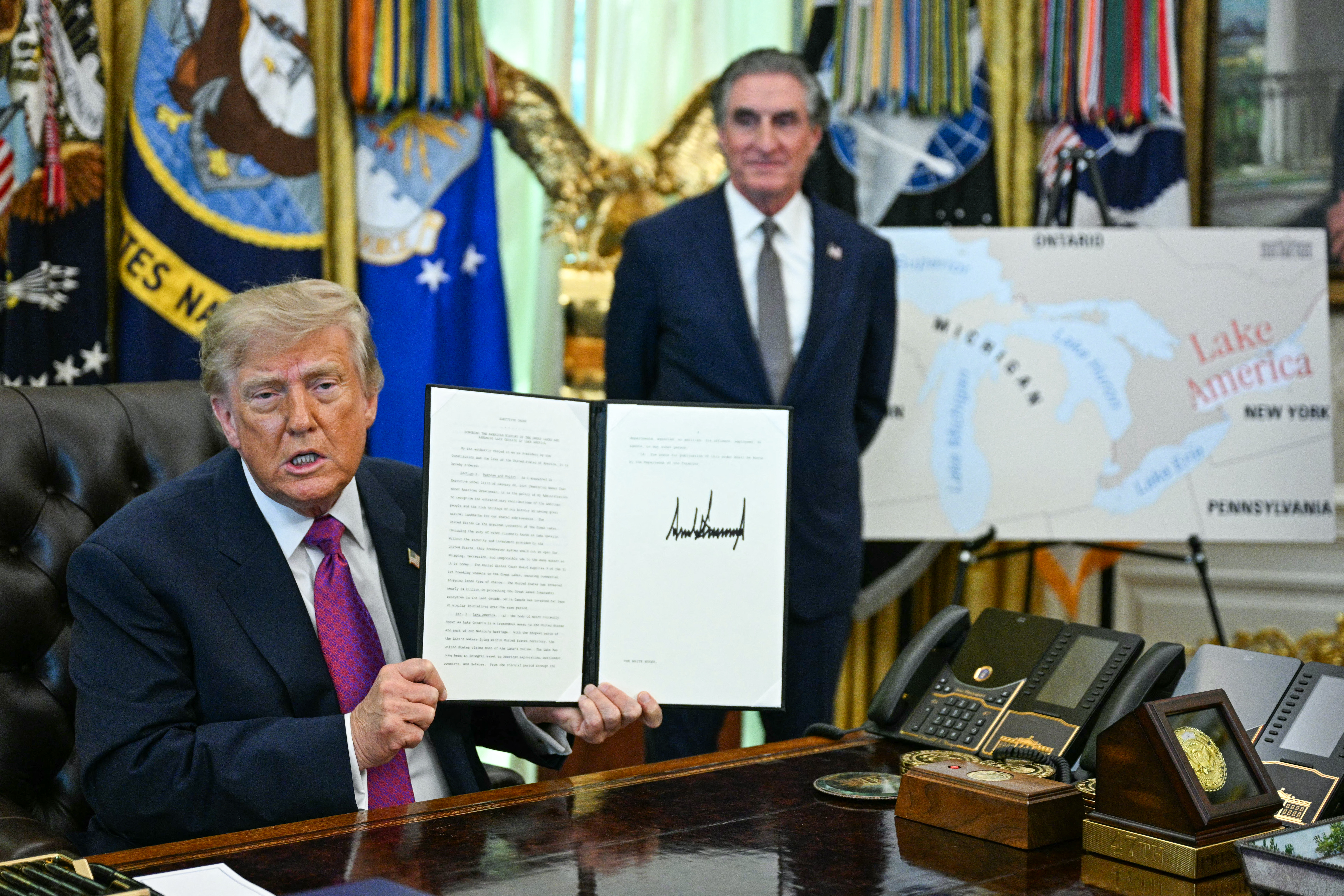 US President Donald Trump, alongside Secretary of the Interior Doug Burgum, displays an executive order he signed that aims to rename Lake Ontario to Lake America in the Oval Office of the White House in Washington, DC, on August 27, 2026.