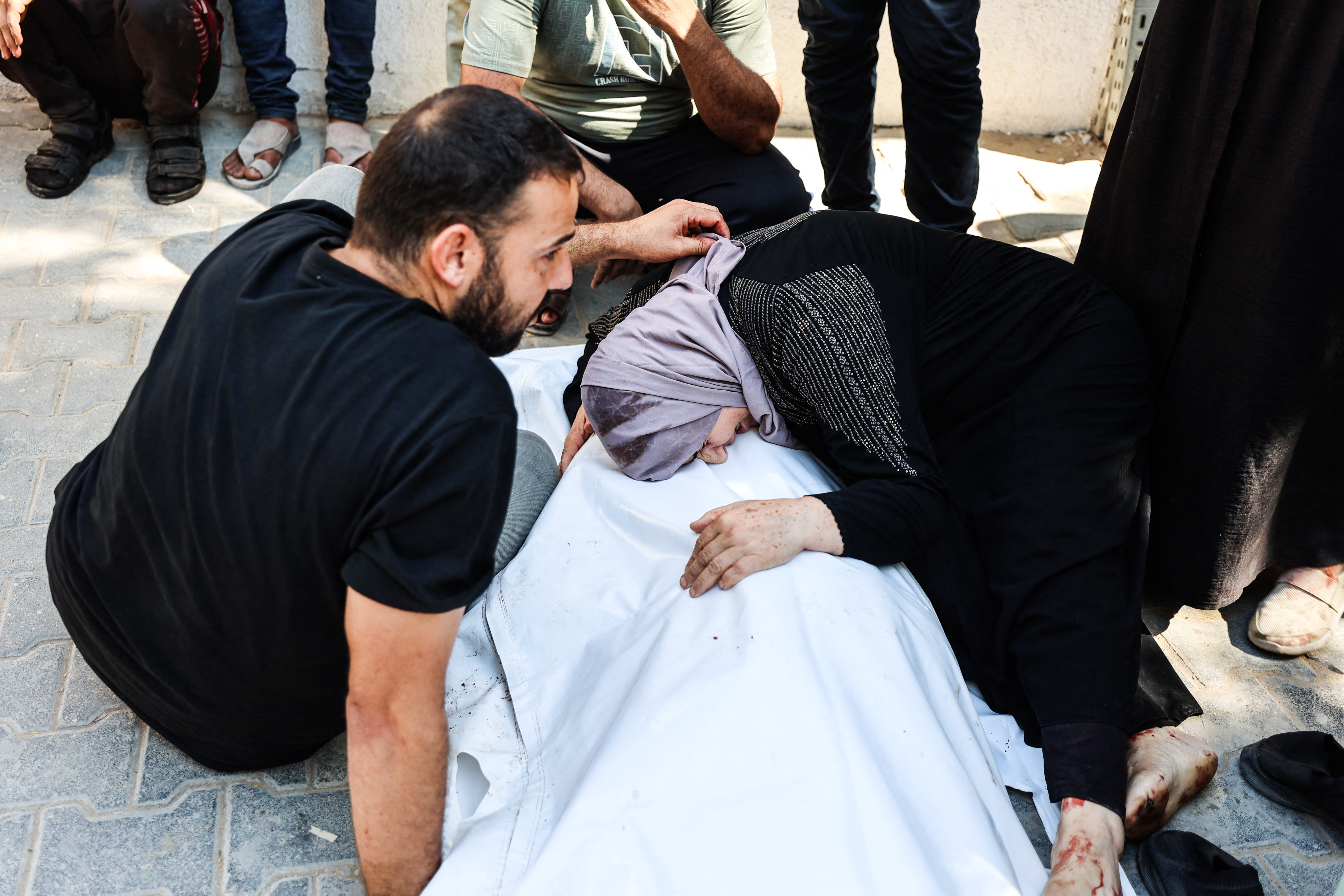 A Palestinian woman grieves over the shrouded body of one of several victims of an Israeli airstrike that targeted a vehicle, as the bodies are taken for burial from the al-Shiffa Hospital in Gaza City, on August 31, 2026.