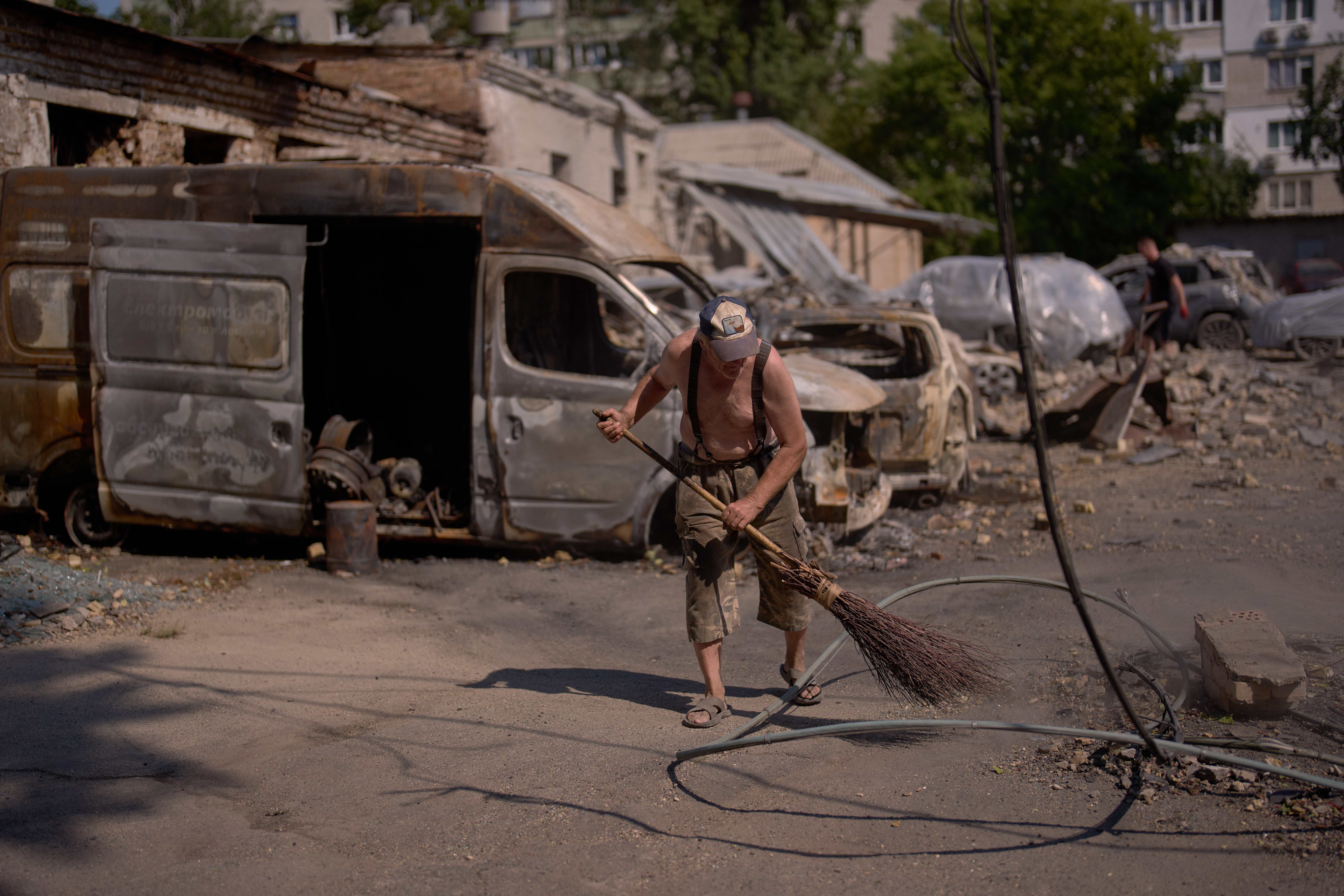 A local resident removes scattered debris next to destroyed vehicles the day after a Russian missile and drone attack in Kyiv