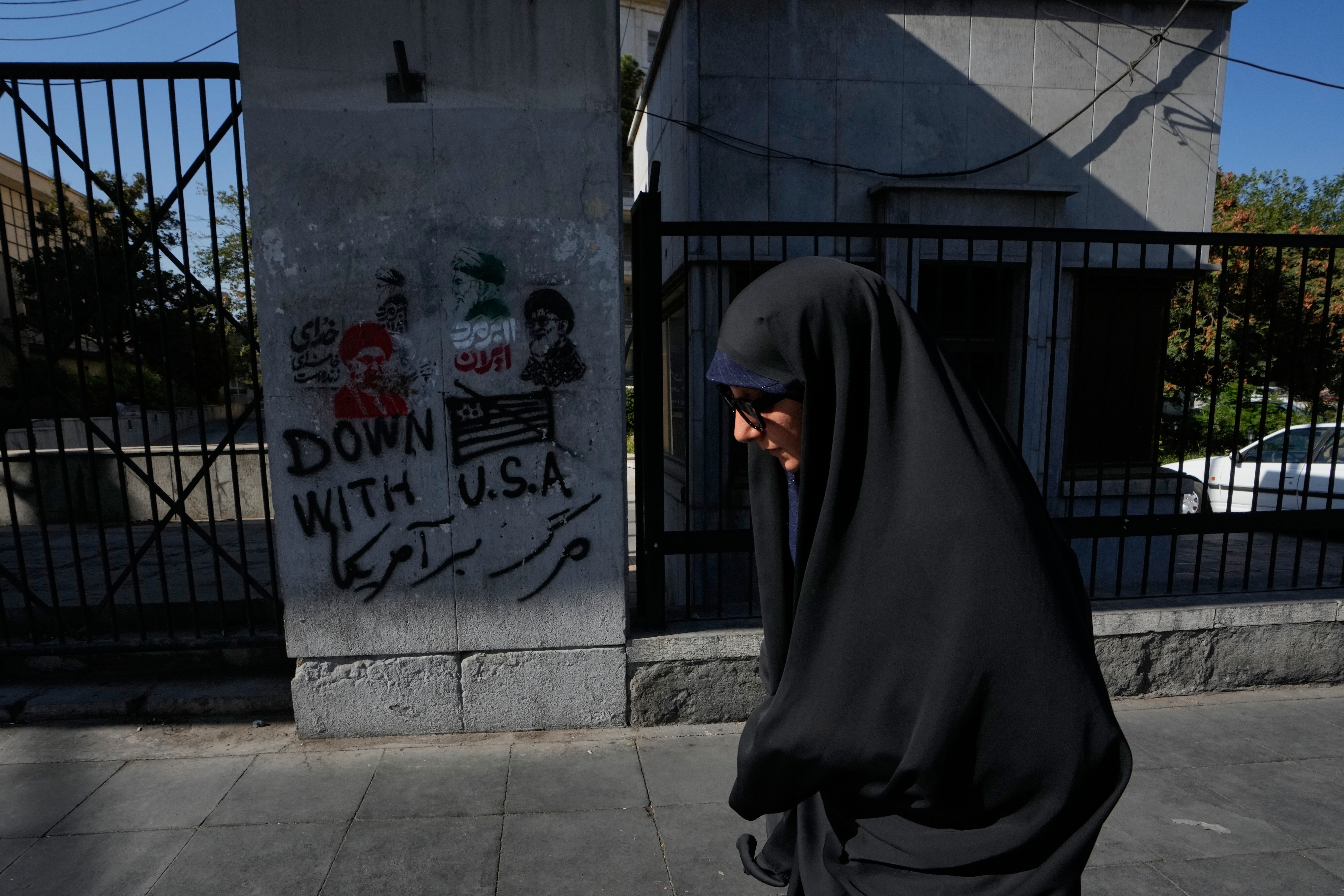 A woman walks past anti-U.S. graffiti and images depicting the late Iranian Supreme Leader Ayatollah Ali Khamenei painted on a wall along Islamic Revolution street in downtown Tehran, Iran, Saturday, Aug. 29, 2026. (AP Photo/Vahid Salemi)