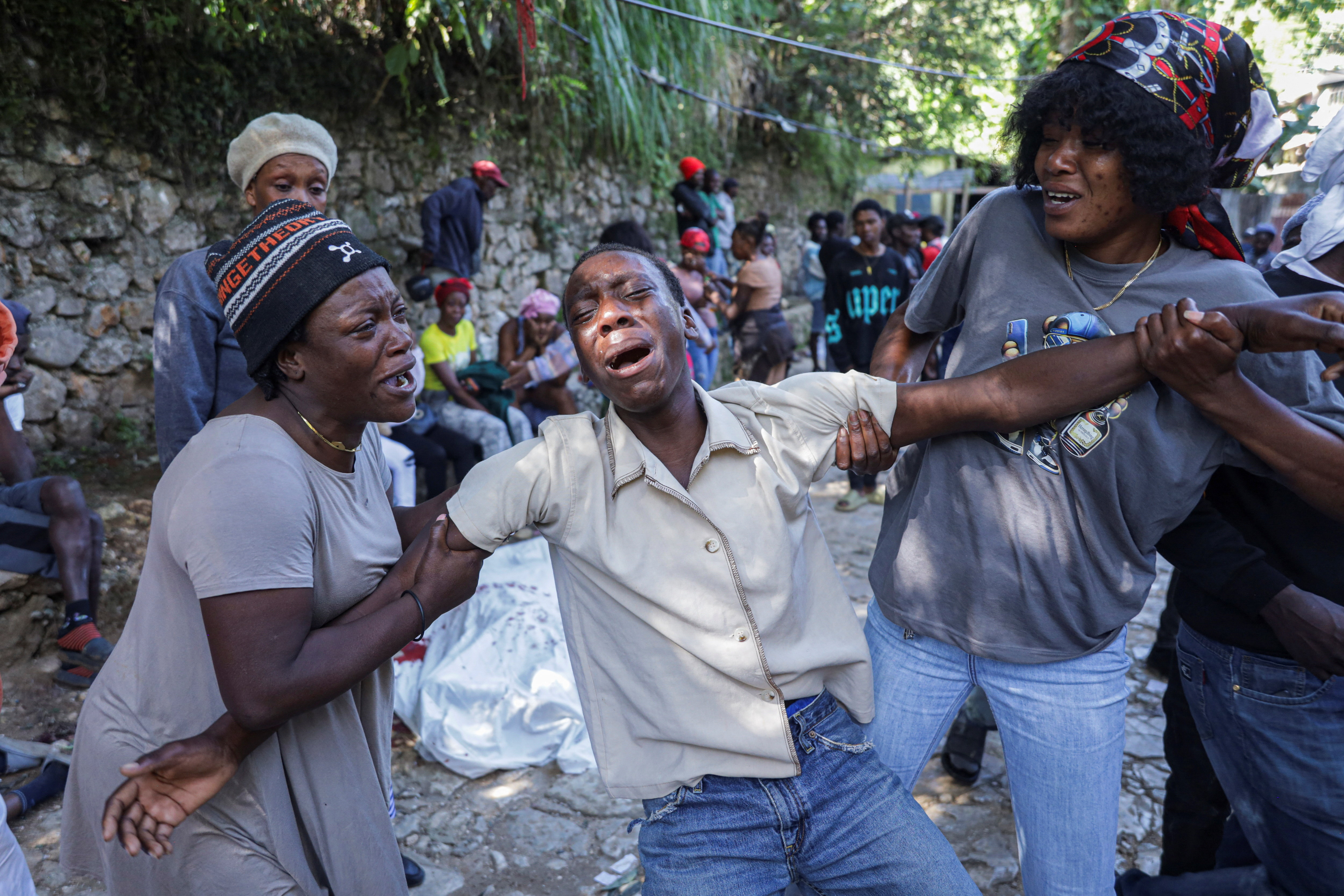 A man mourns next to the covered body of a person killed during an overnight raid by an armed gang, on the outskirts of Port-au-Prince, in Kenscoff, Haiti, August 24, 2026. REUTERS/Patrice Noel
